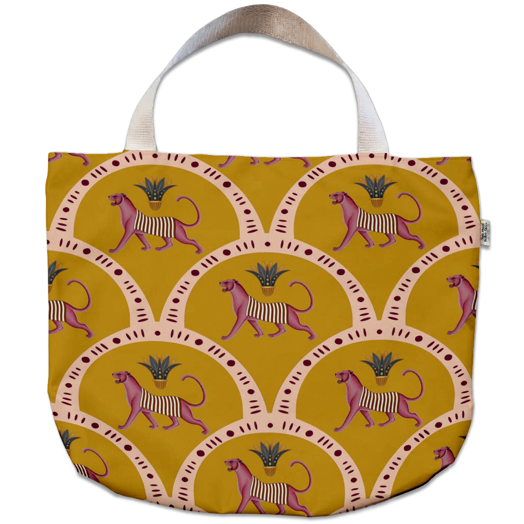 A tote bag featuring a repeating pattern of pink and purple striped lions inside beige arches on a mustard yellow background, with a light beige fabric handle.