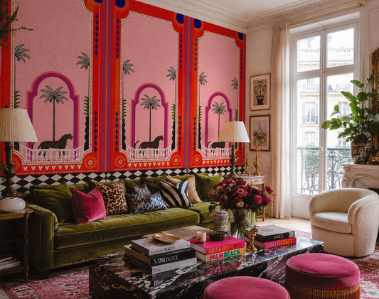 A luxurious living room featuring a bold pink and red patterned wallpaper as the main focal point, paired with a deep green velvet sofa, pink velvet ottomans, and a marble coffee table.