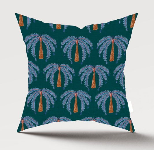 A square throw pillow featuring a repeating palm tree pattern on a dark teal background, with light blue-gray fronds and orange trunks, shown against a light gray studio background.