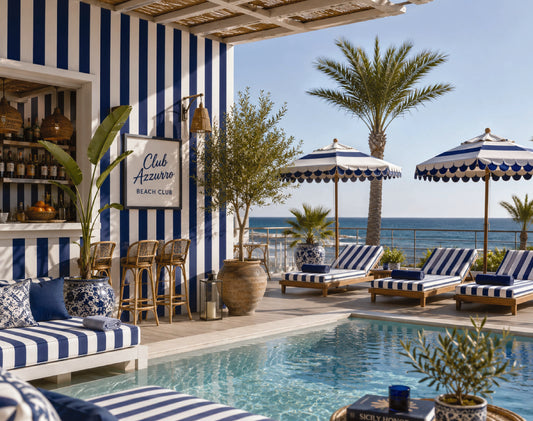 A luxurious outdoor poolside lounge area with blue and white striped seating, umbrellas, palm trees, and a sign reading Club Azzaro Beach Club, set against a clear ocean view.