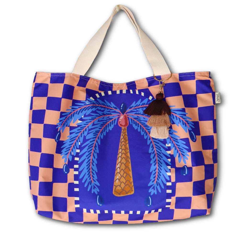 A tote bag featuring a blue and peach checkerboard pattern, a central blue palm tree illustration, and cream-colored shoulder straps, shown against a plain white background.