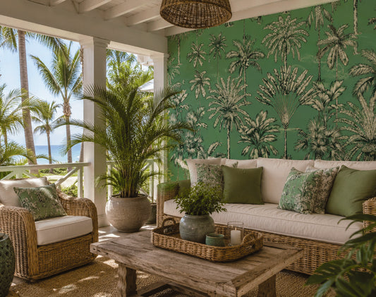 A tropical-themed living room featuring a vibrant green wall covered in palm tree pattern wallpaper, styled with a white cushioned sofa, green pillows, a rustic wooden coffee table, and a large potted palm plant.