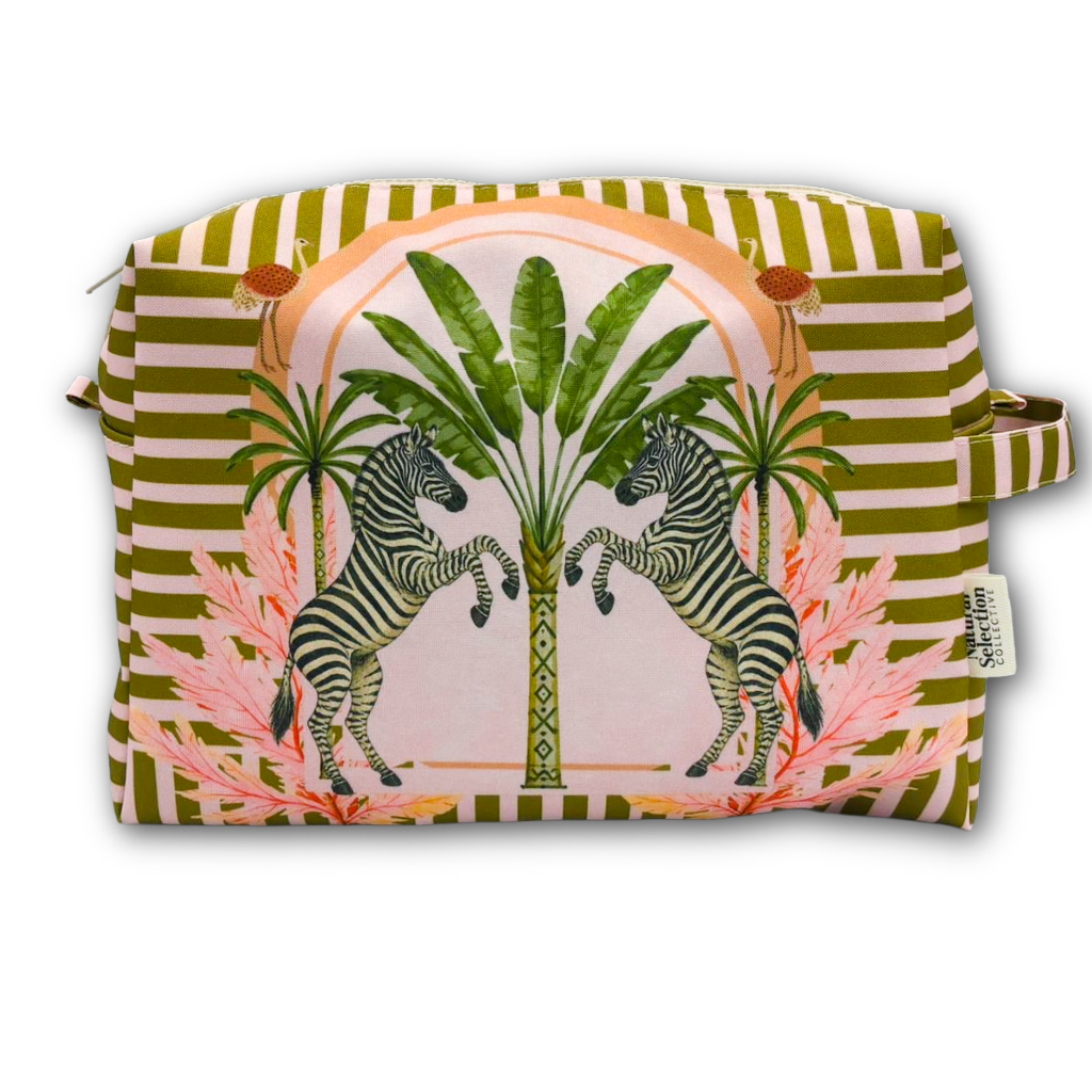 A rectangular zippered pouch with a colorful tropical print featuring two rearing zebras, palm trees, and pink tropical leaves, set against a background of olive green and white stripes. A small fabric tag on the right side reads 'The Art of Travel'.