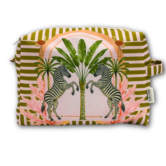 A rectangular zippered pouch with a colorful tropical print featuring two rearing zebras, palm trees, and pink tropical leaves, set against a background of olive green and white stripes. A small fabric tag on the right side reads 'The Art of Travel'.