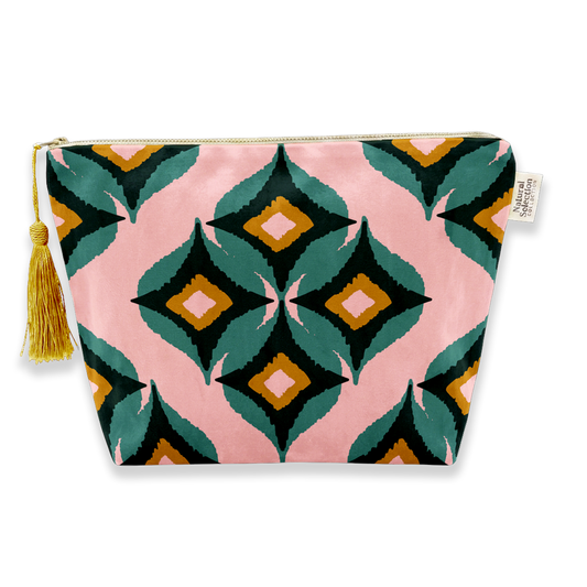 A rectangular zippered pouch with a pink background and a bold geometric diamond pattern in teal, black, mustard yellow, and white. A gold zipper runs across the top, and a gold tassel is attached to the left side.