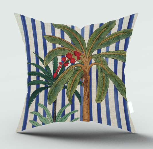 A square decorative throw pillow featuring a tropical palm tree design with green leaves, brown trunks, and red flowers over a blue and cream vertical stripe background, shown on a light gray studio background.