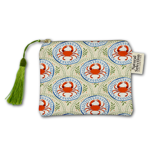 A small zippered pouch with a repeating crab pattern in red, blue, and green on a cream background, featuring a green tassel zipper pull and a side tag reading Natural Selection.