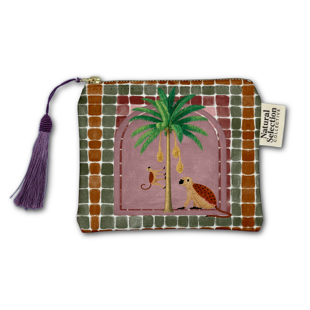 A rectangular zip pouch with a decorative embroidered design featuring a palm tree, a monkey, and a turtle on a dusty pink background, bordered by a green and brown checkered pattern. It has a purple tassel zipper pull and a 'Natural Selection' brand tag.