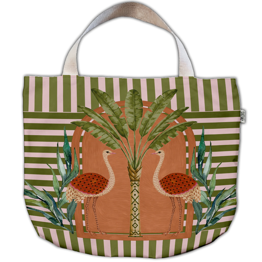A waterproof 
tote bag with green and white horizontal stripes, featuring a central illustration of two flamingos in front of a palm tree. The bag has light beige shoulder straps and a decorative purple tassel charm on the left side, shown against a plain white background.