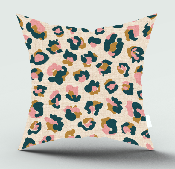 A square throw pillow with a textured linen-like fabric, featuring an abstract leopard print pattern in pink, dark teal, and mustard brown on a warm beige background, shown against a light gray studio backdrop.