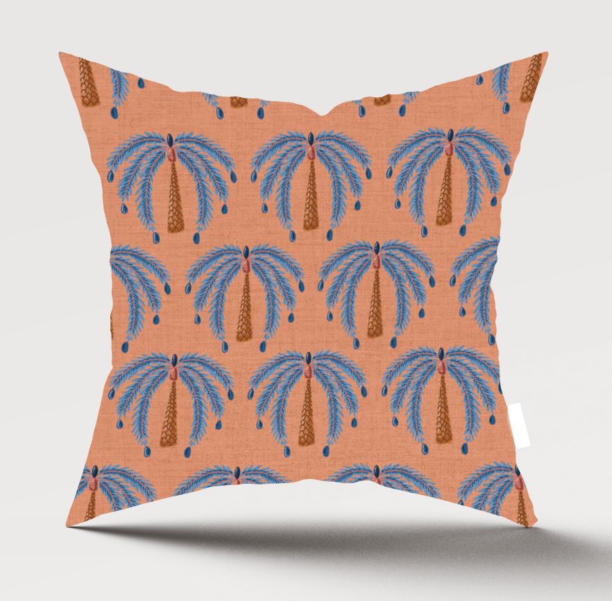 A square decorative throw pillow with a terracotta orange background and a repeating palm tree pattern in blue and brown, shown against a light gray studio background.