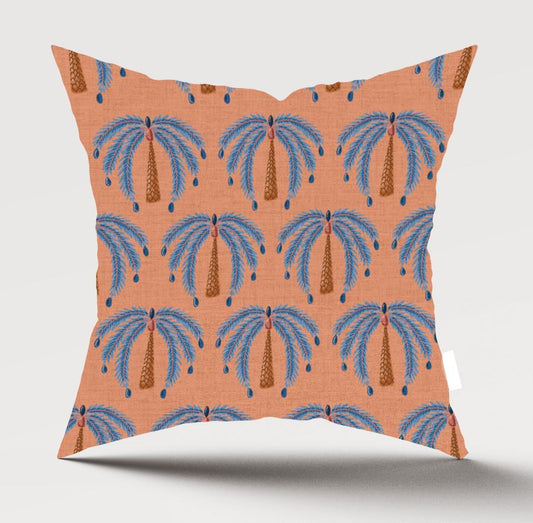 A square decorative throw pillow with a terracotta orange background and a repeating palm tree pattern in blue and brown, shown against a light gray studio background.