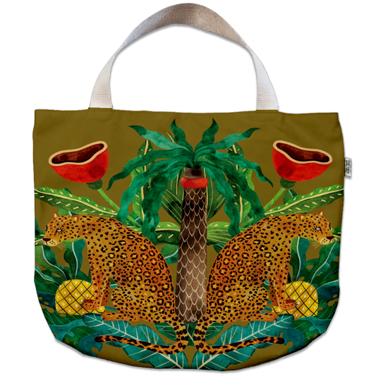 A tote bag with a detailed jungle and safari illustration featuring two leopards, a palm tree, red bowls, pineapples, and a snake on an olive green background, with white shoulder straps.