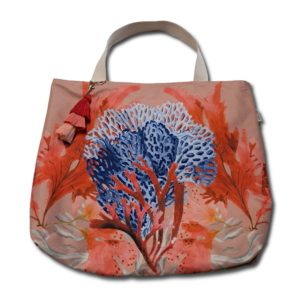 A canvas tote bag featuring a vibrant coral print with a large blue and orange sea fan motif on a dusty pink background, complete with beige shoulder straps and a red tassel charm.