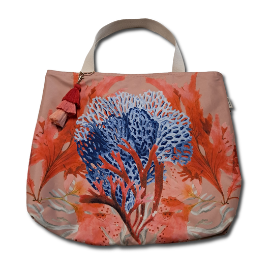 A canvas tote bag featuring a vibrant coral print with a large blue and orange sea fan motif on a dusty pink background, complete with beige shoulder straps and a red tassel charm.