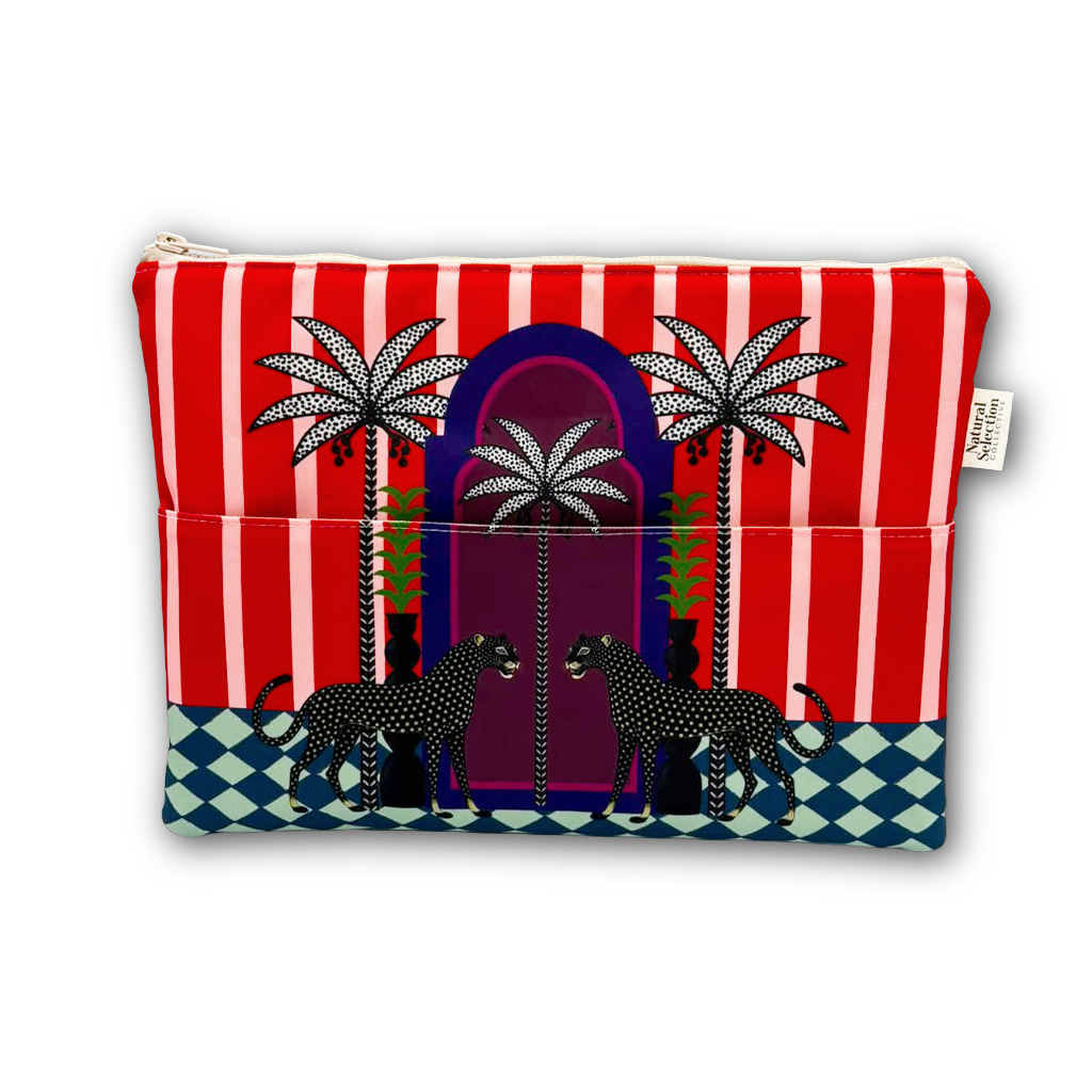 A zippered cosmetic pouch featuring a vibrant, stylized African wax print design with red and white vertical stripes, palm trees, a purple archway, two black-and-white spotted cheetahs, and a blue-and-white checkered base.