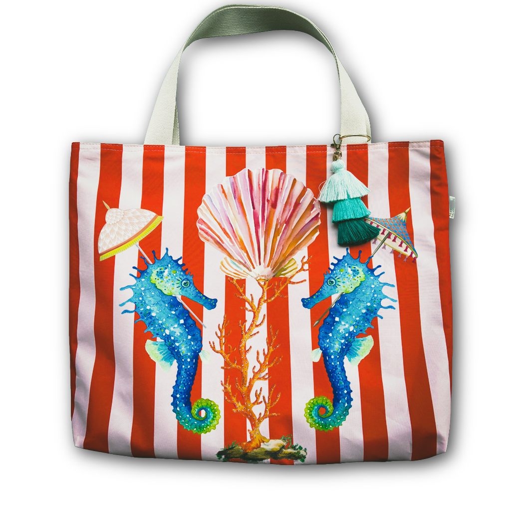 A tote bag with a red and white striped background, featuring two blue seahorses, a pink and orange seashell, and two small umbrella charms hanging from the side handles.