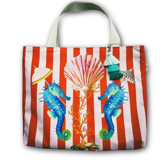 A tote bag with a red and white striped background, featuring two blue seahorses, a pink and orange seashell, and two small umbrella charms hanging from the side handles.