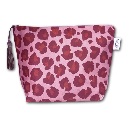 A pink zippered pouch with a dark red and burgundy leopard print pattern, featuring a matching tassel zipper pull and a small white brand tag that reads 'Natural Living'.