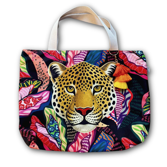 A tote bag featuring a colorful, vibrant pattern of a leopard's face surrounded by tropical flowers on a dark background, with white shoulder straps.