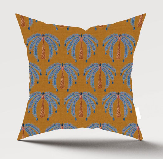 A square throw pillow featuring a repeating palm tree pattern on a mustard yellow background, with blue fronds and orange trunks, shown against a light gray studio background.