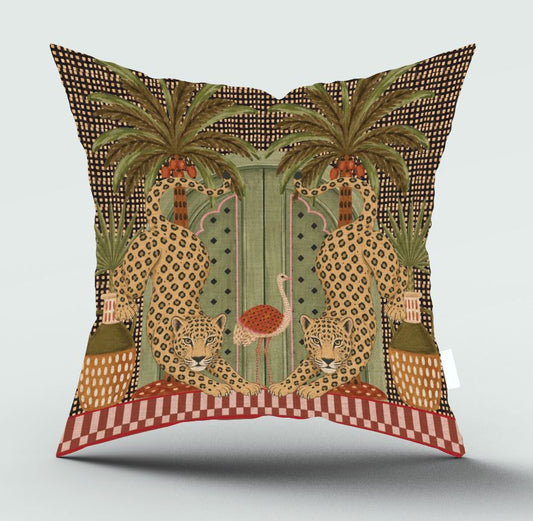 A square decorative throw pillow featuring a detailed vintage-style illustration of two leopards, two palm trees, and a central green door, with a red and white checkered border at the bottom, shown against a light gray background.