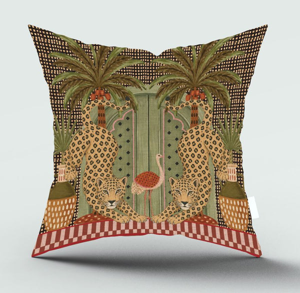 A square decorative throw pillow featuring a detailed vintage-style illustration of two leopards, two palm trees, and a central green door, with a red and white checkered border at the bottom, shown against a light gray background.