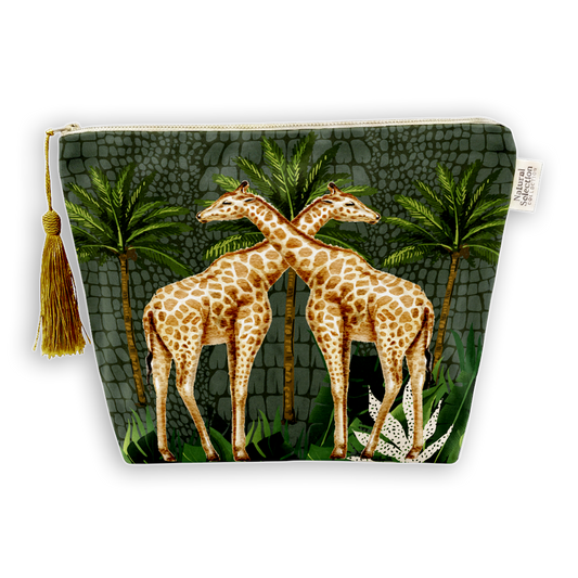 A zippered cosmetic pouch featuring a printed design of two giraffes standing in front of palm trees on a dark textured background, with a gold tassel on the left side.