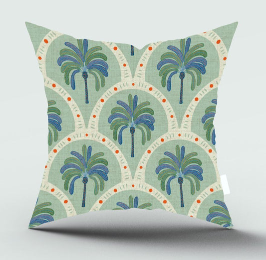 A square throw pillow featuring a retro bohemian palm tree pattern in shades of blue, green, and orange on a sage green and cream background, shown against a neutral gray studio backdrop.
