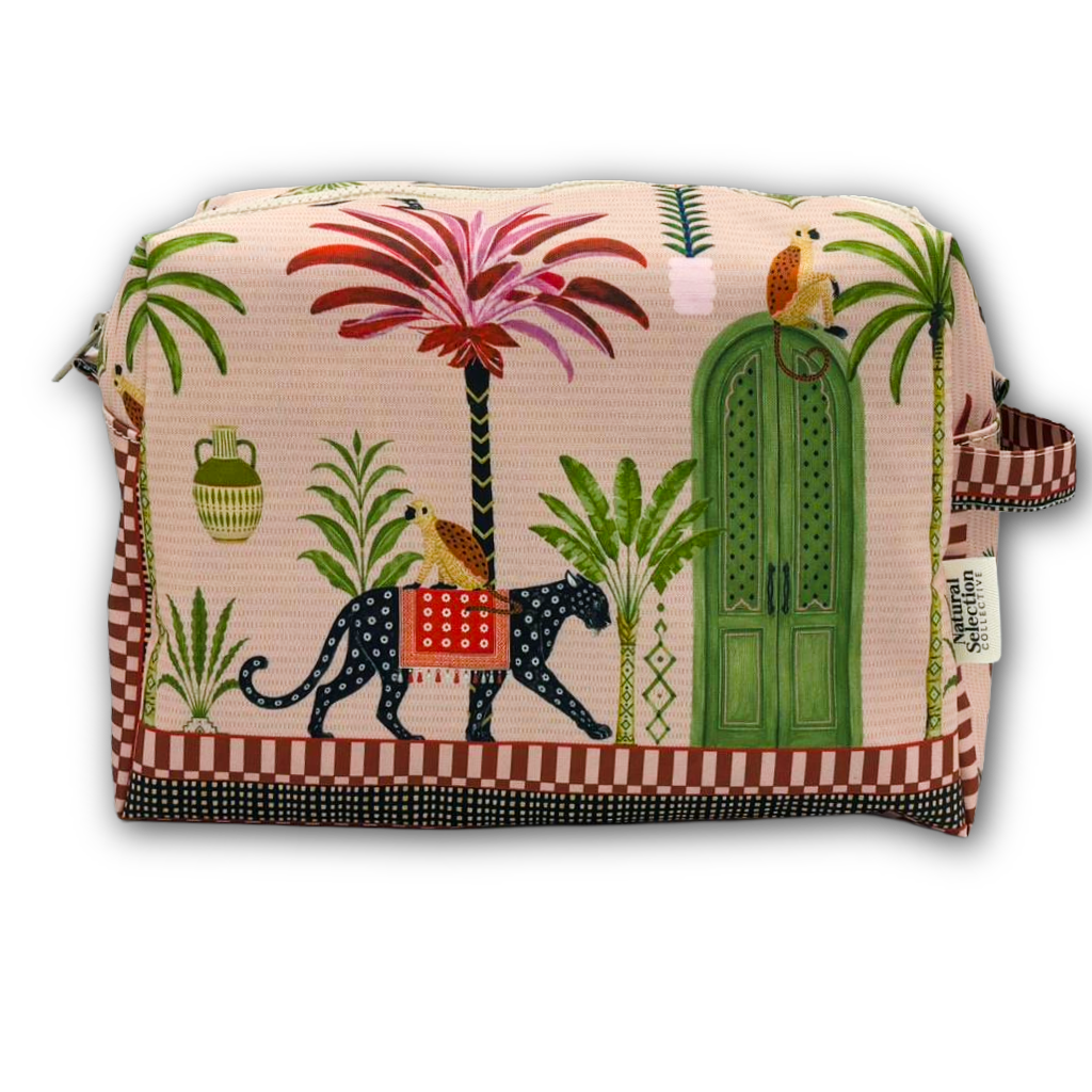 A rectangular zippered cosmetic pouch featuring a vibrant, multicolored tropical and African-inspired print with palm trees, a green door, a leopard, and birds on a light pink background, set against a plain white studio background.