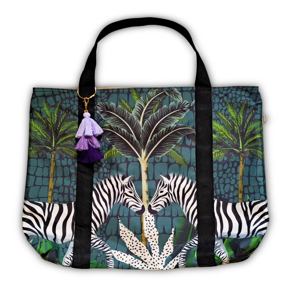 A tote bag featuring a tropical jungle print with palm trees, zebras, and a purple tassel charm, shown against a plain white background.
