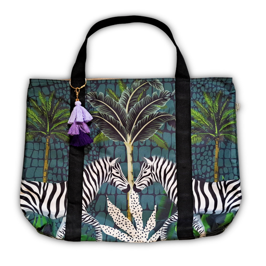 A tote bag featuring a tropical jungle print with palm trees, zebras, and a purple tassel charm, shown against a plain white background.