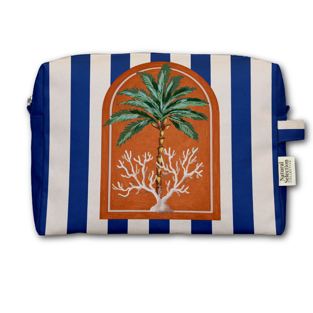 A rectangular zippered pouch with vertical blue and off-white stripes, featuring a central arched illustration of a green palm tree and white coral on an orange-brown background. A small side tag reads Natural Living.