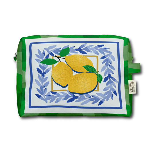 A green and white patterned zippered pouch featuring a central illustration of two yellow lemons framed by blue leafy laurel branches on a white background. A small fabric brand tag on the right side reads 'The Artisanal Shop'.