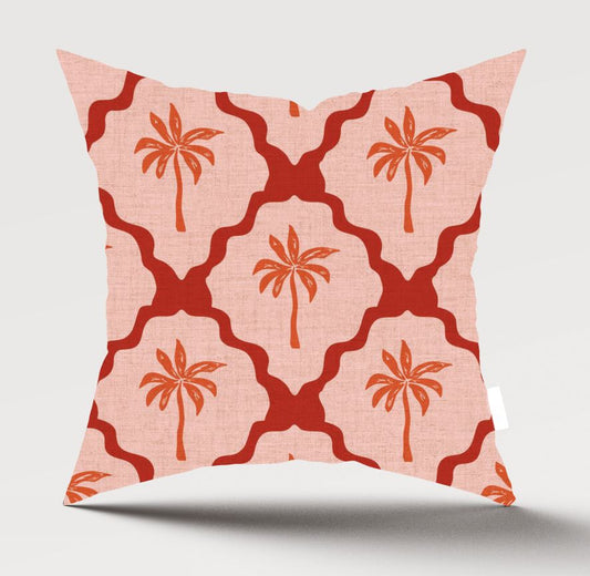 A square throw pillow with a coral pink and red geometric trellis pattern and palm tree motifs, shown against a light gray background.
