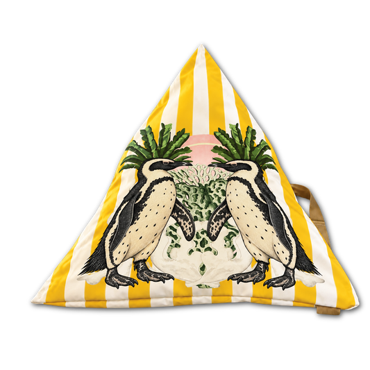 A triangular floor cushion with a yellow and white striped background, featuring an illustration of two penguins standing on a white shell with green leaves and pink sky details in the center.