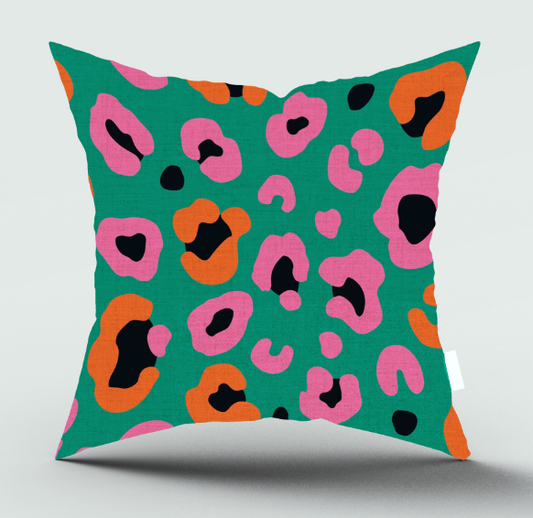 A square throw pillow with a vibrant green background and a bold leopard-style print in pink, orange, and black, shown against a light gray background.